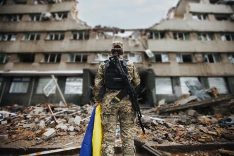 oekrainse soldate met de rug naar de camera kijkend naar een ingestort gebouw met vlag in de hand